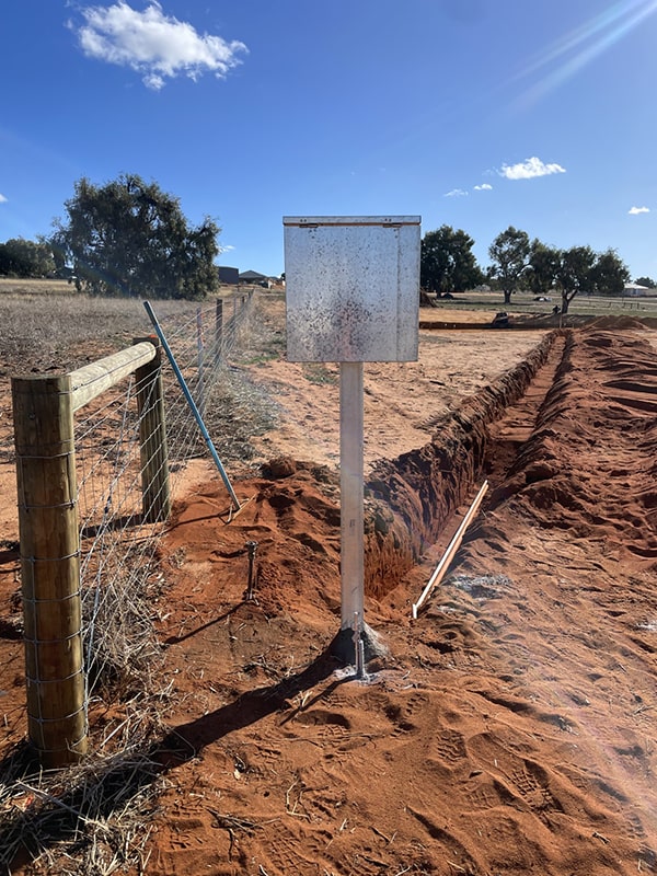 Subdivision electrical meterbox installation by Dynamic Group in progress on a rural red dirt property in Western Australia, with trenching and fencing visible under a clear blue sky.